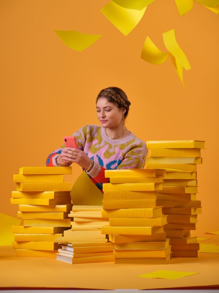 Girl looking at phone on a pile of yellow books