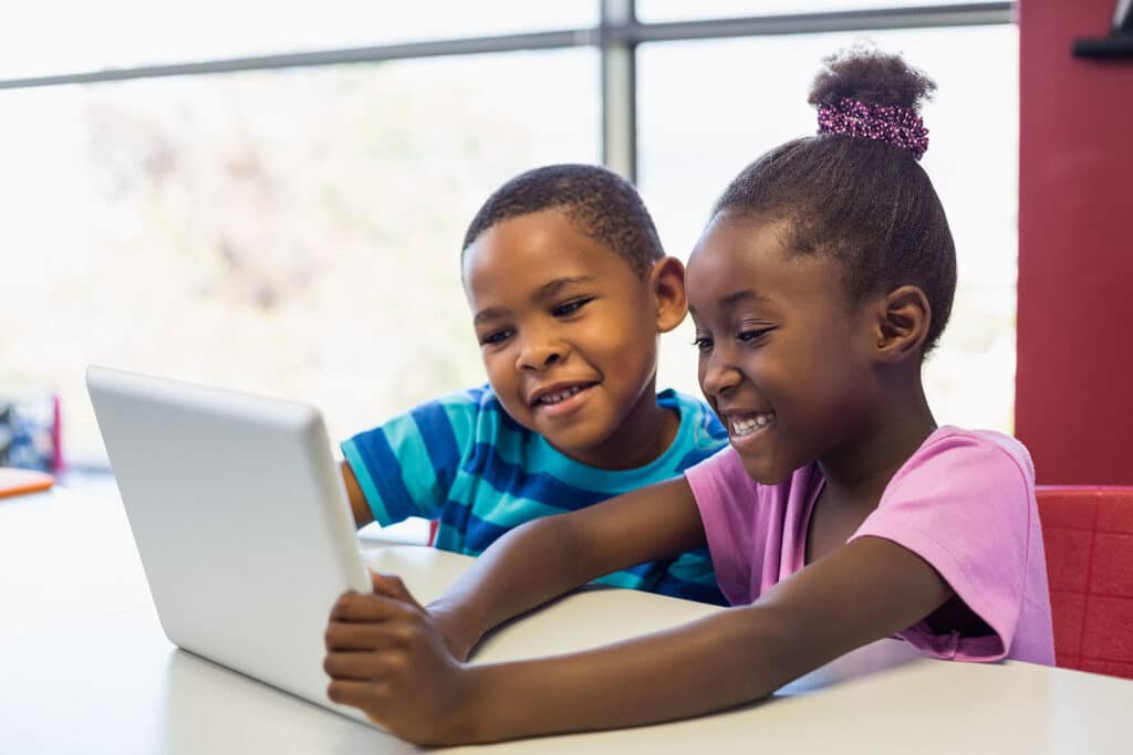 two small children smiling while they look at a tablet