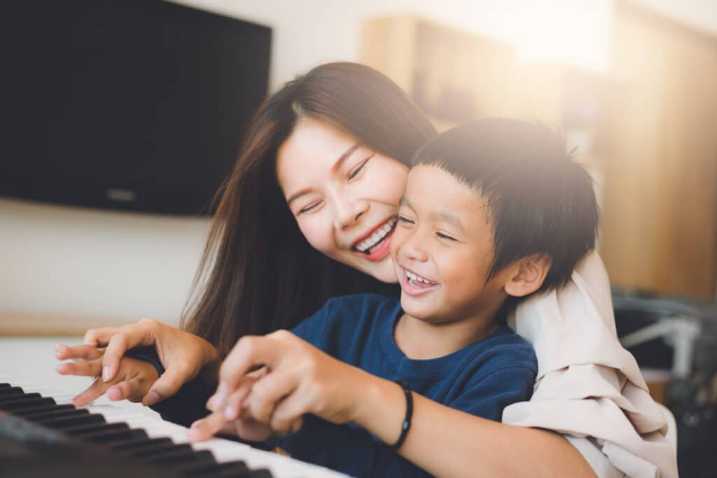 mother and small son on her lap smile and play piano