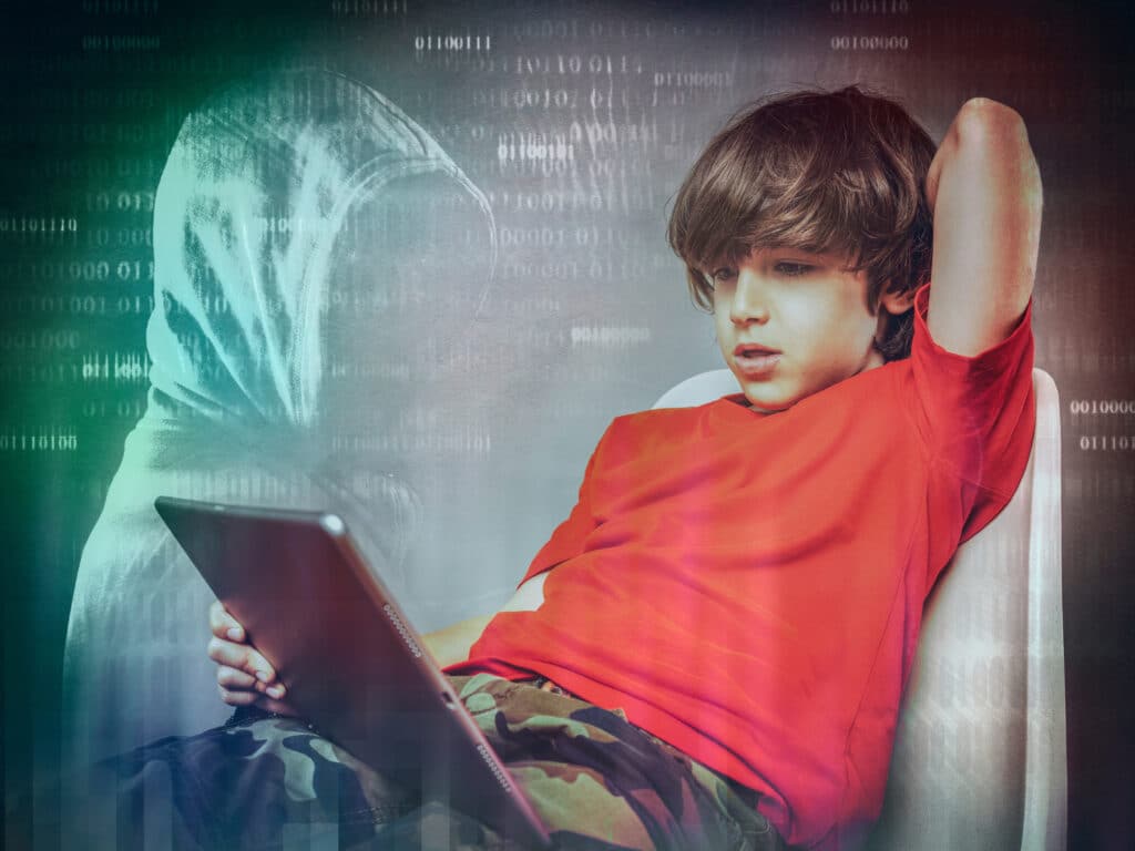 young boy on ipad with hooded figure in the background