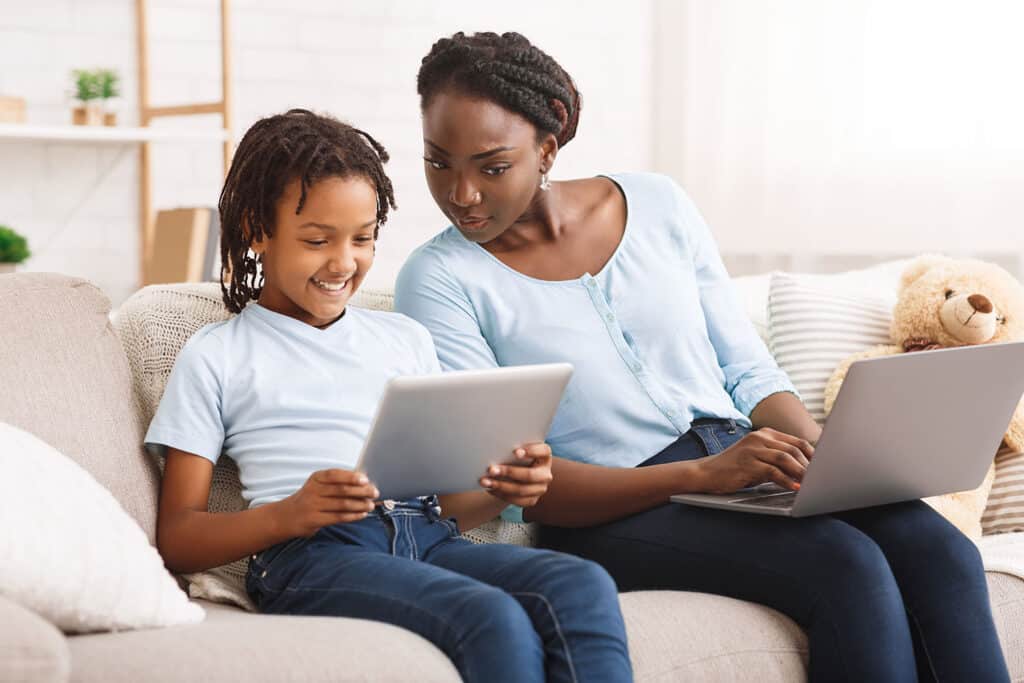 mother on laptop looking concerned over at child on tablet