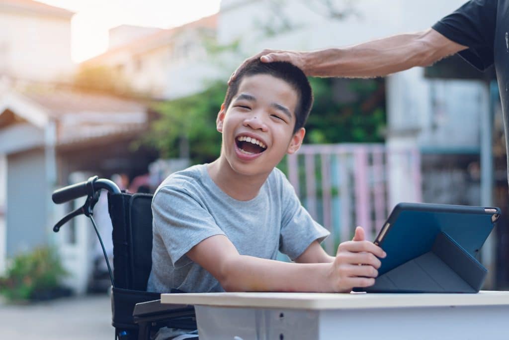 boy in wheelchair smiling with tablet device