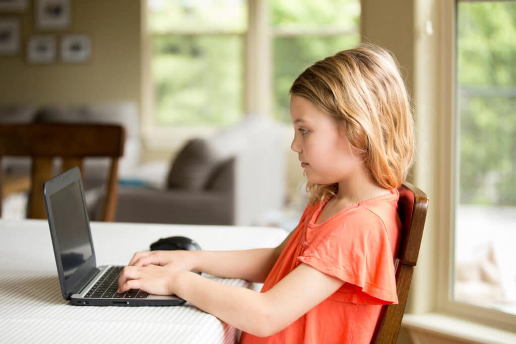 little girl on laptop at dining table