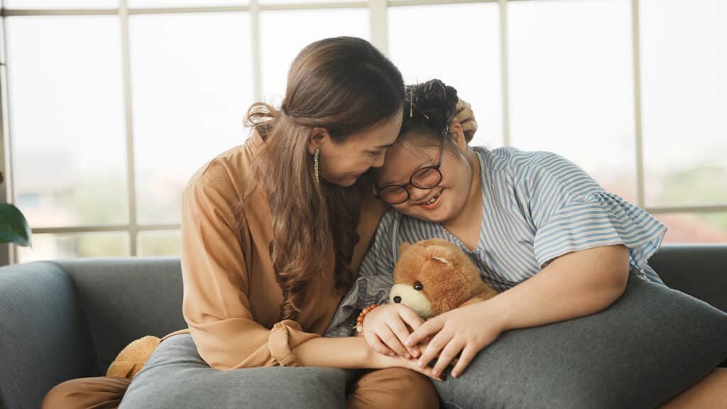woman hugging smiling girl with glasses and teddy bear