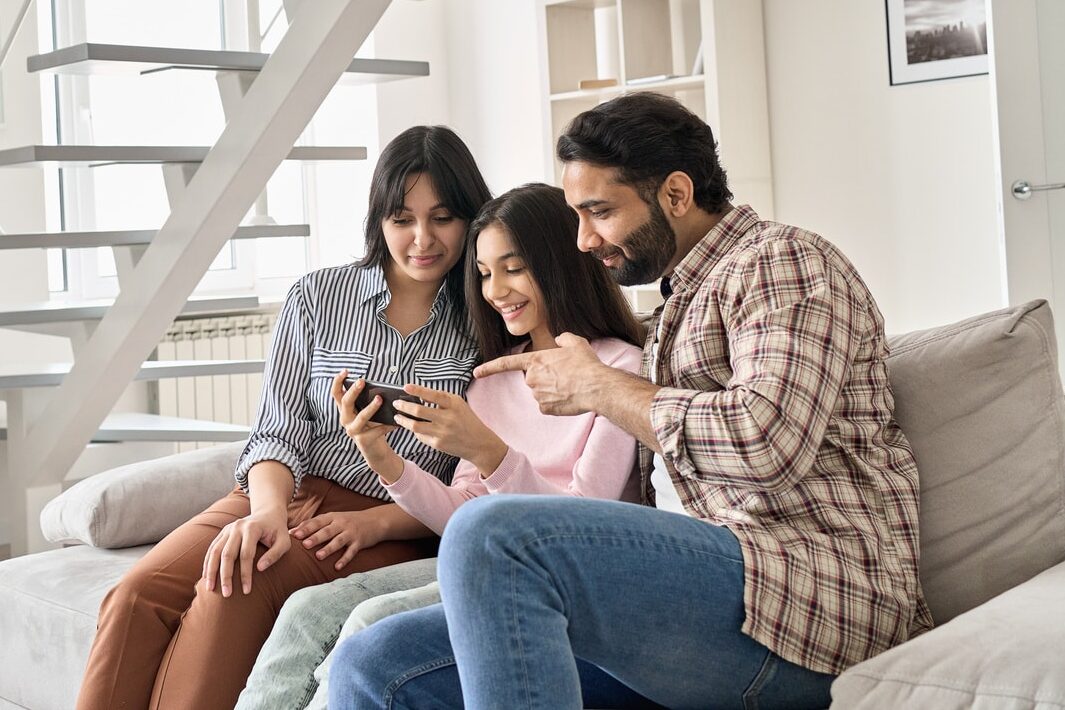 parents looking at cellphone with teen daughter on couch