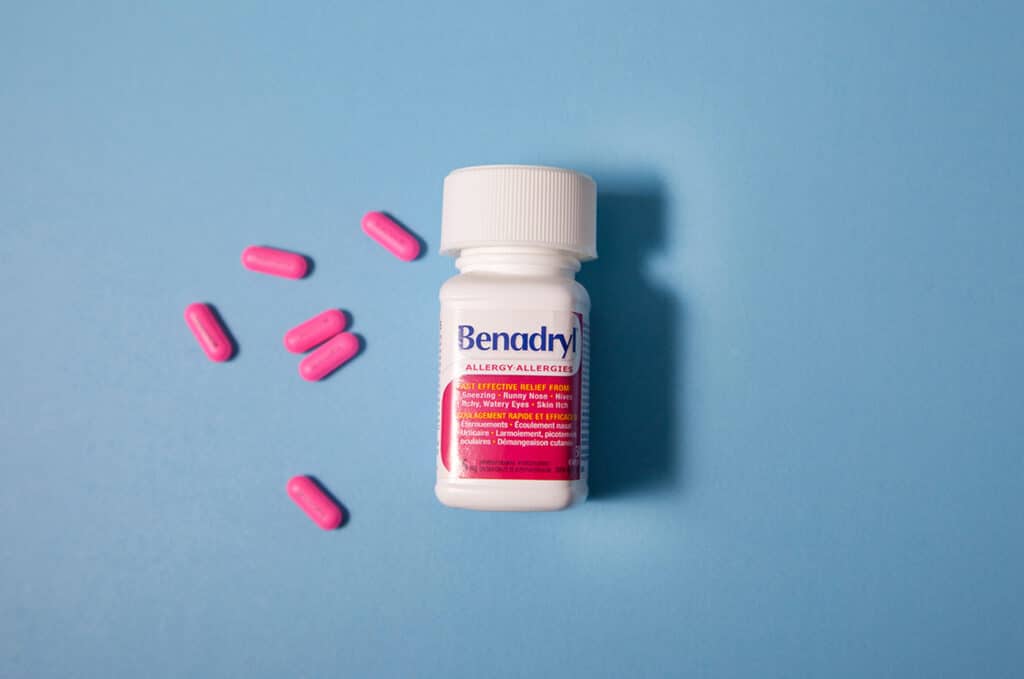bottle of benadryl with pink pills lying to the side of it