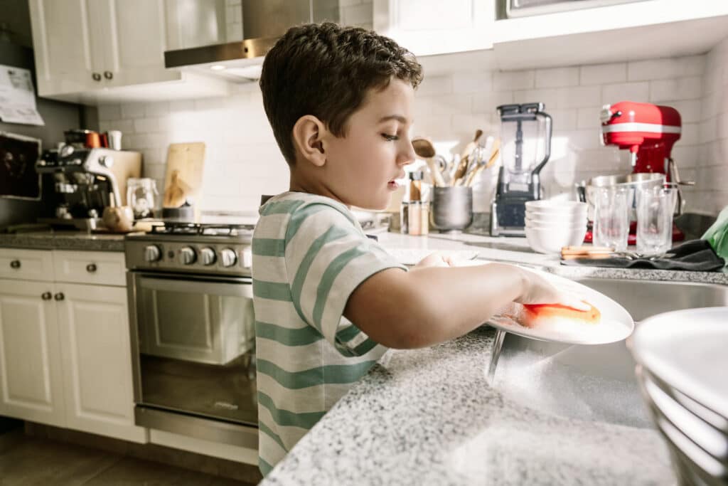 young boy washes dishes