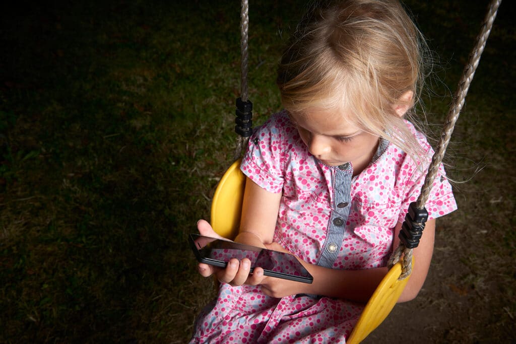 small girl on swing looking at a cellphone in the dark