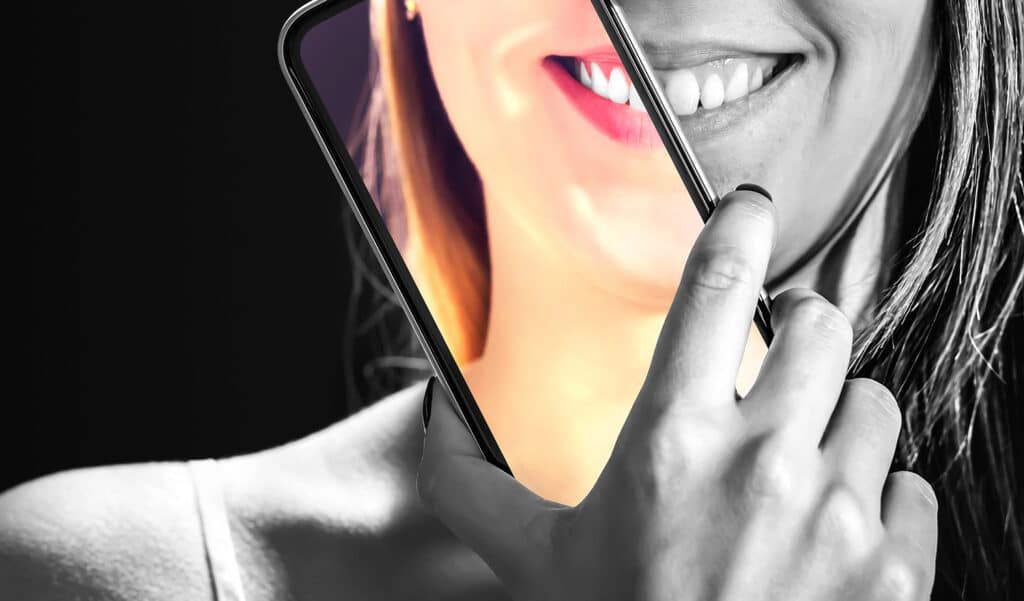 black and white photo of woman holding a phone to her face and the screen is in full color