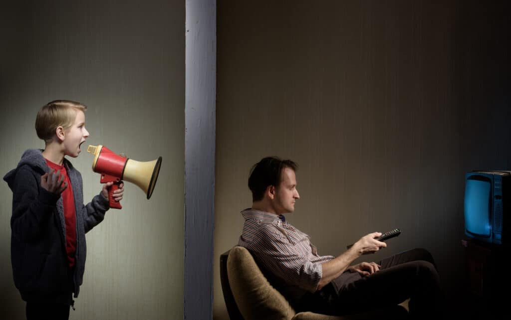 son with megaphone stying to yell through a wall to aloof father watching television