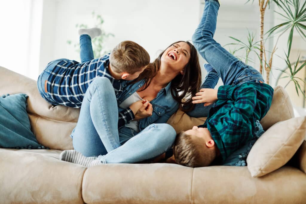 laughing mother wrestling with two sons on couch