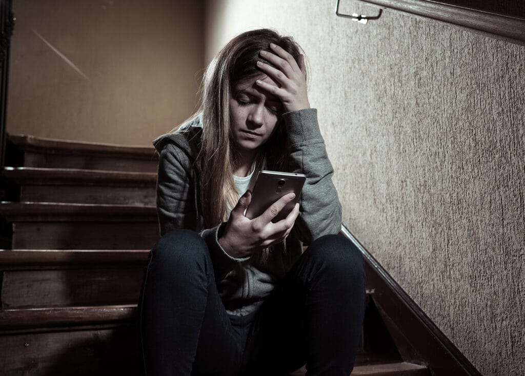 young girl upset in stairwell looking at phone
