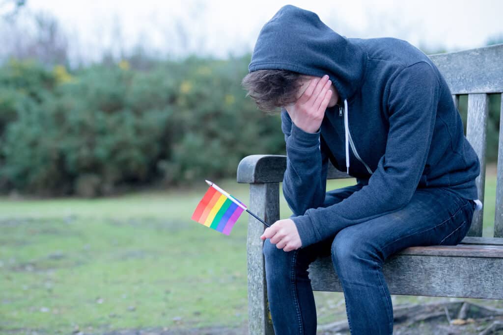 LGBTQ+ youth holding pride flag with face in hand