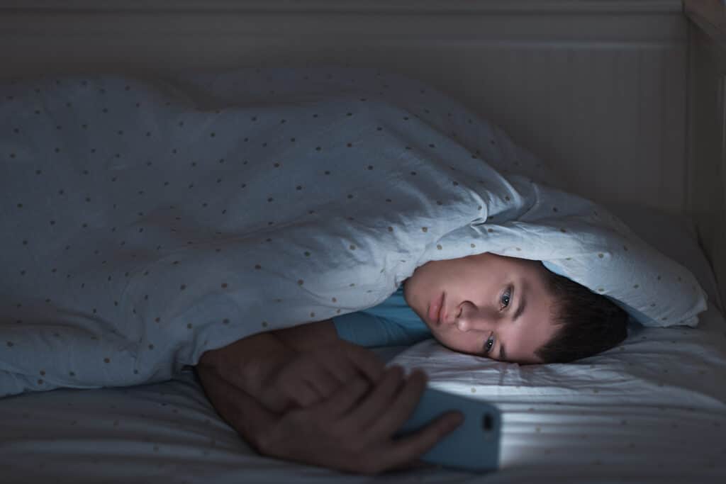 teen boy in bed on his phone in the dark