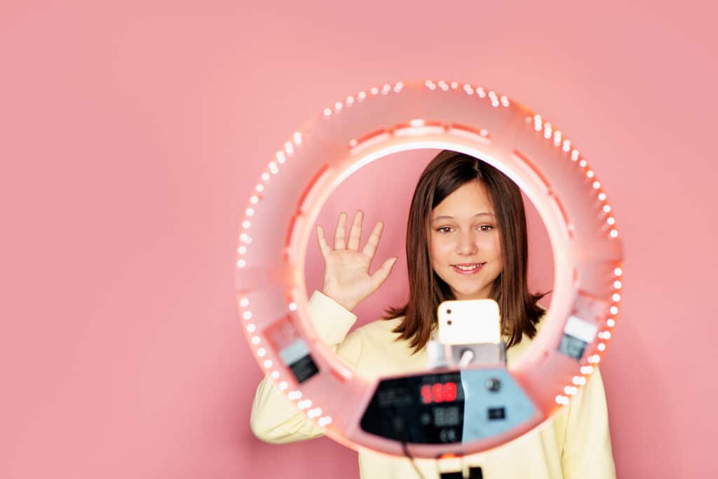 young girl waving at smartphone with ring light framing her face